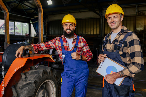 Smiling colleagues standing next to the tractor and making repair plan