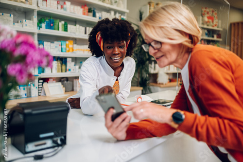 Senior woman showing smartphone screen to an african american female pharmacist photo