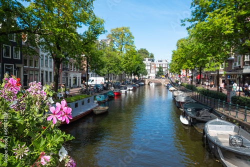 View of an Amsterdam street with canal, typical Dutch architecture, boats and flowers.