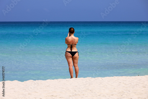 Wall Mural Woman in bikini standing with smartphone on a tropical sandy beach