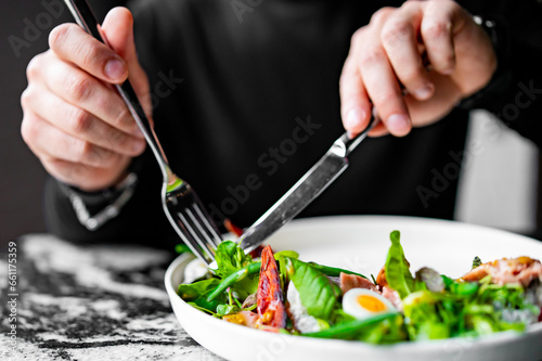 Hands of a man with a fork and knife eat Salad nicoise. Tuna, with green beans, tomatoes, potatoes and a vinaigrette mustard dressing in white plate