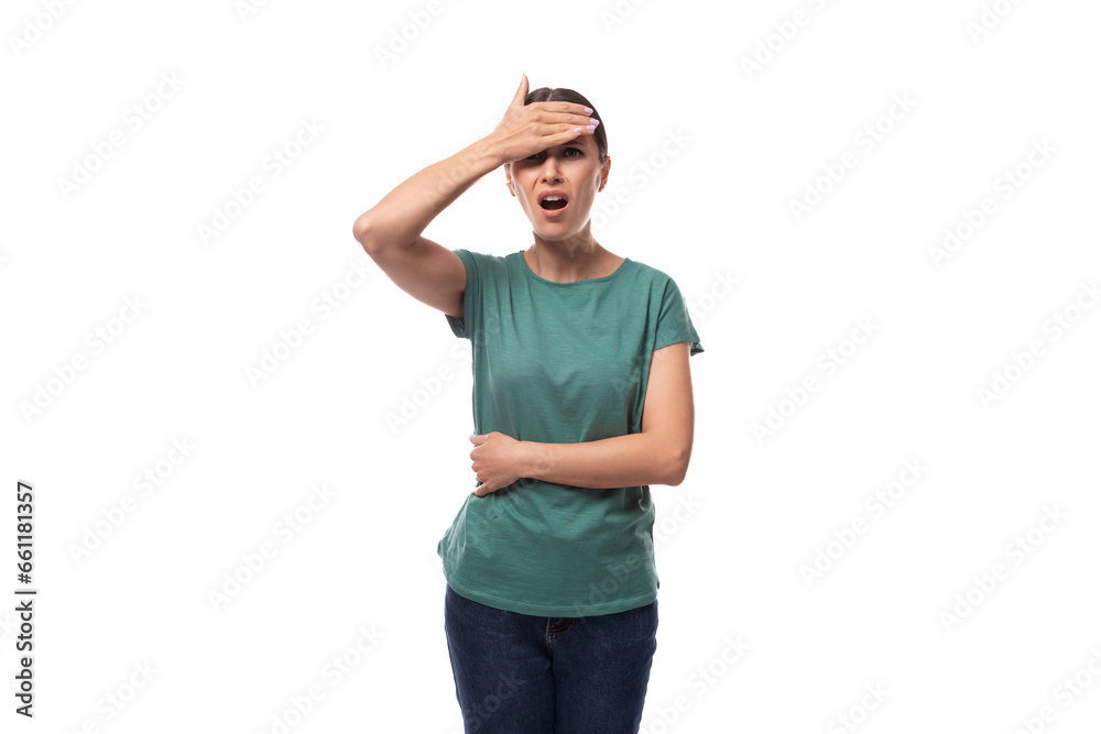 30 year old brunette woman with ponytail dressed in a green basic T-shirt is worried and holding her head 30 year old brunette woman with ponytail dressed in a green basic T-shirt is worried and holding her head
