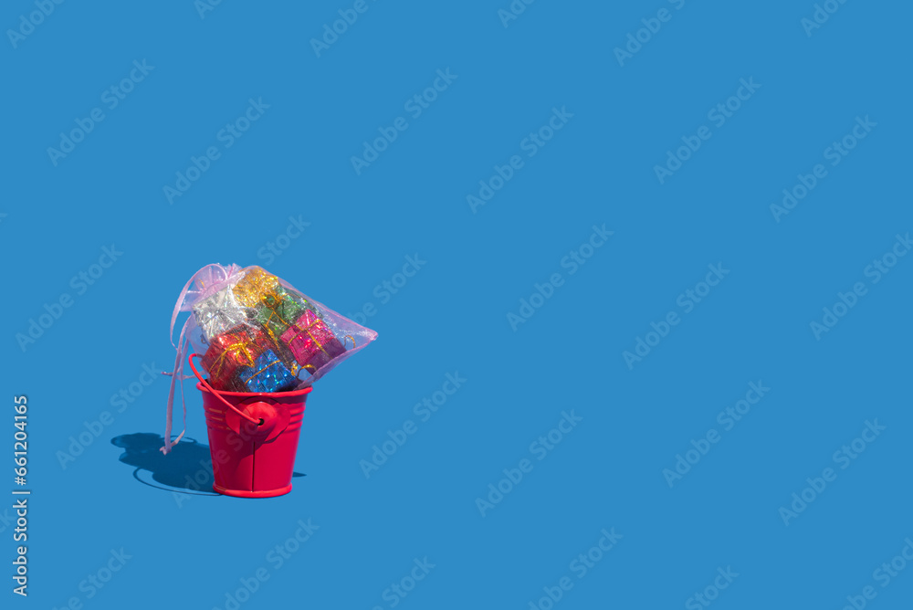 Red bucket full of gift boxes on blue background. Christmas holiday concept.