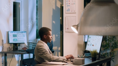 African american manager asking employee to show him company project tasks progress in modern office during nightshift. Management executive crosschecking documents at work photo