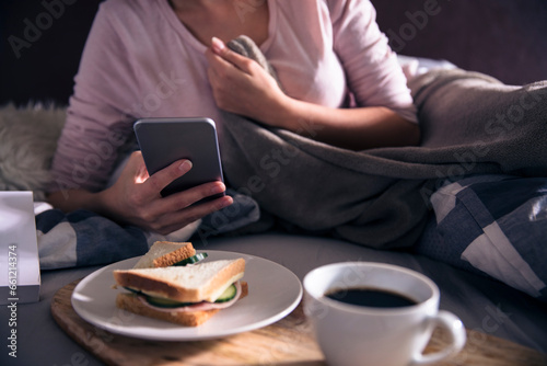 Close up of a young woman using a smartphone having breakfast at bed