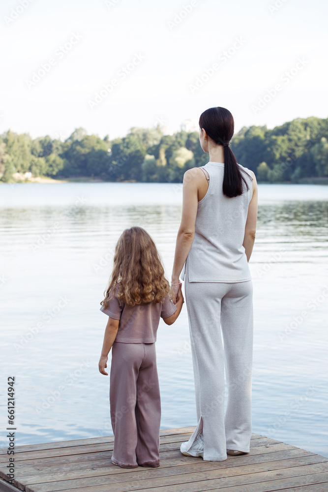 A young mother and her five-year-old daughter watch the fish in the lake, standing on the bridge.