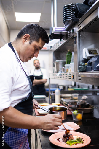 Latino chef finishing the fillet in the kitchen of his restaurant. His partner is looking in the background