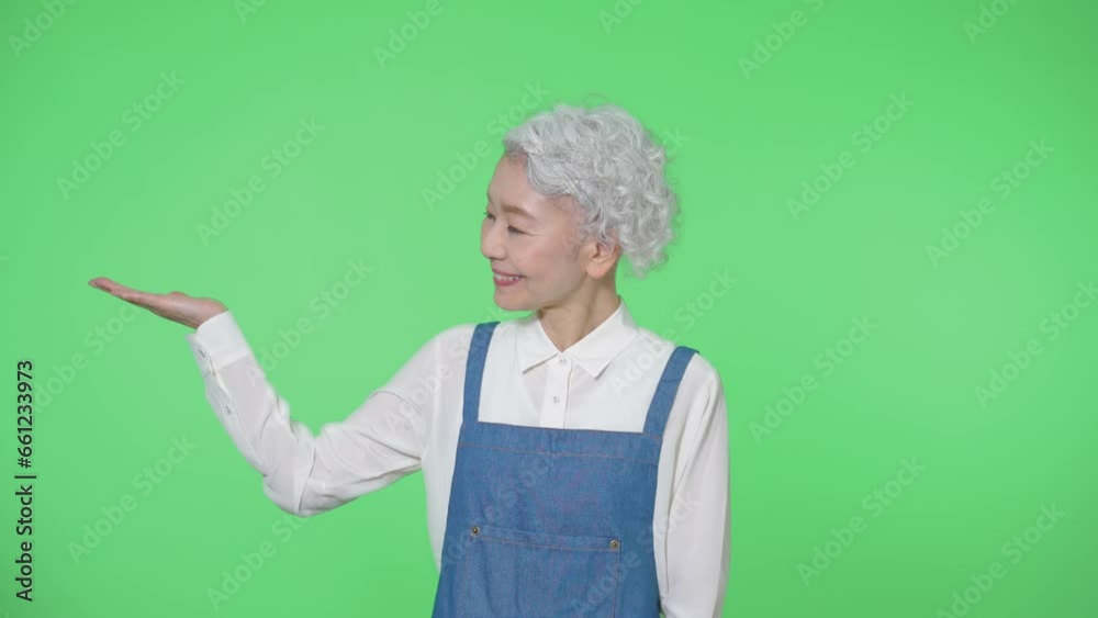 案内するエプロンをつけたシニア女性　クロマキー合成用グリーンバック