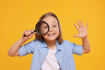 Cute little girl looking through magnifier on yellow background