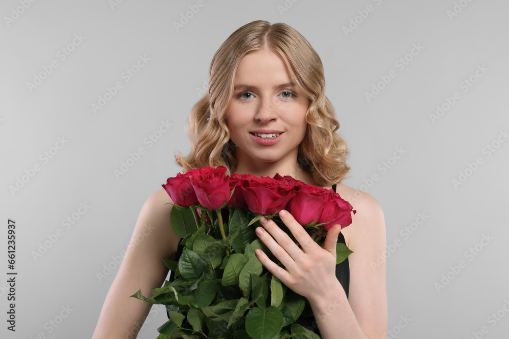 Beautiful woman with blonde hair holding bouquet of red roses on light grey background Beautiful woman with blonde hair holding bouquet of red roses on light grey background