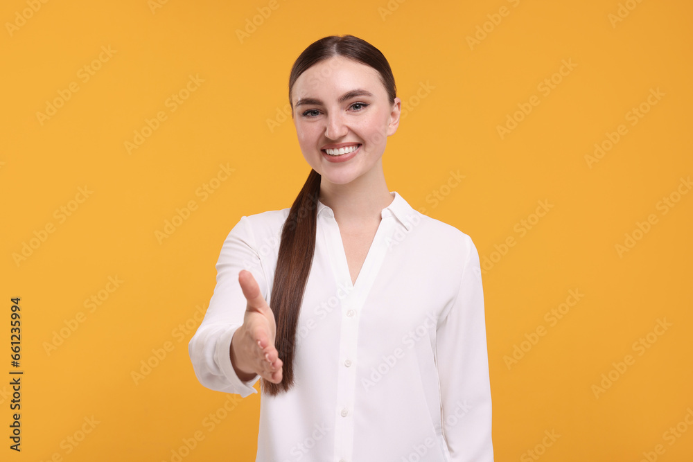 Smiling woman welcoming and offering handshake on orange background Smiling woman welcoming and offering handshake on orange background