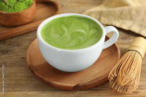 Cup of fresh matcha latte and bamboo whisk on wooden table, closeup