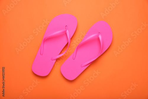 Stylish pink flip flops on orange background, top view