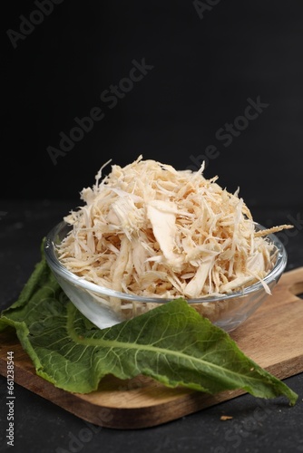 Grated horseradish in bowl, leaf and board on black table, closeup. Space for text