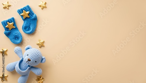 Baby accessories concept. Top view of blue teether knitted teddy-bear toy tiny socks and gold stars on isolated pastel beige background with copy space