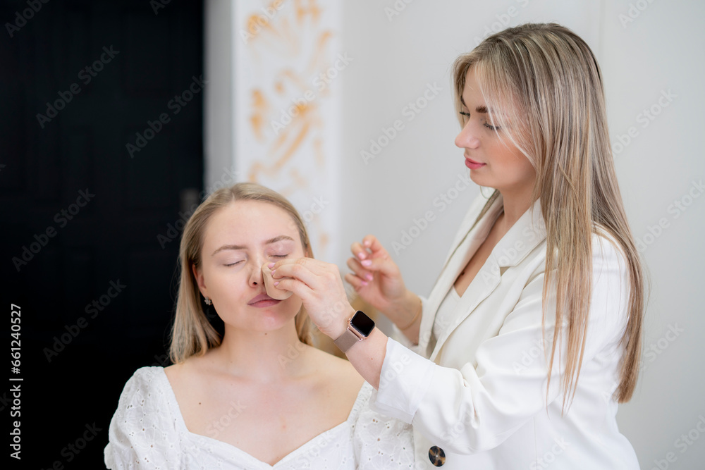 visagiste applies foundation with a sponge on the young woman's face visagiste applies foundation with a sponge on the young woman's face