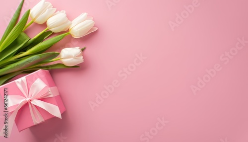 Mother's Day concept. Top view of stylish pink gift box with ribbon bow and bouquet of tulips on isolated pink background with copy space