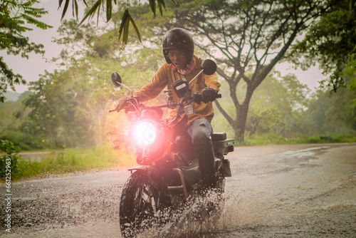 man riding small endurom motorcycle crossing shallow creek among rain falling at forest photo