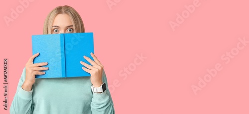 Shocked young woman with book on pink background with space for text