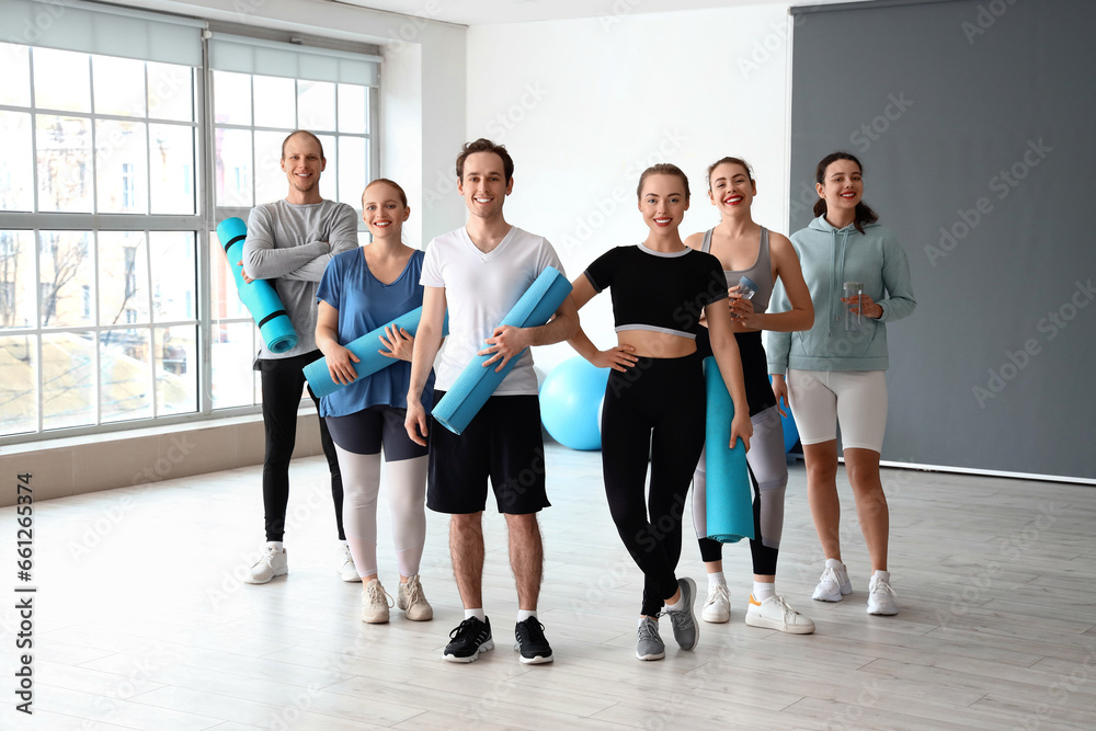 Fototapeta premium Group of sporty young people with fitness mats and bottles in gym