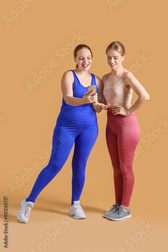 Sporty young women with smartphone on beige background