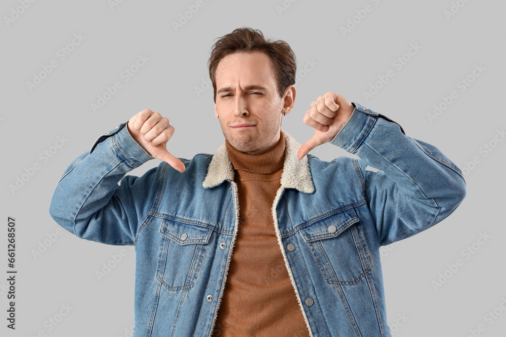 Displeased young man showing thumbs-down on light background Displeased young man showing thumbs-down on light background