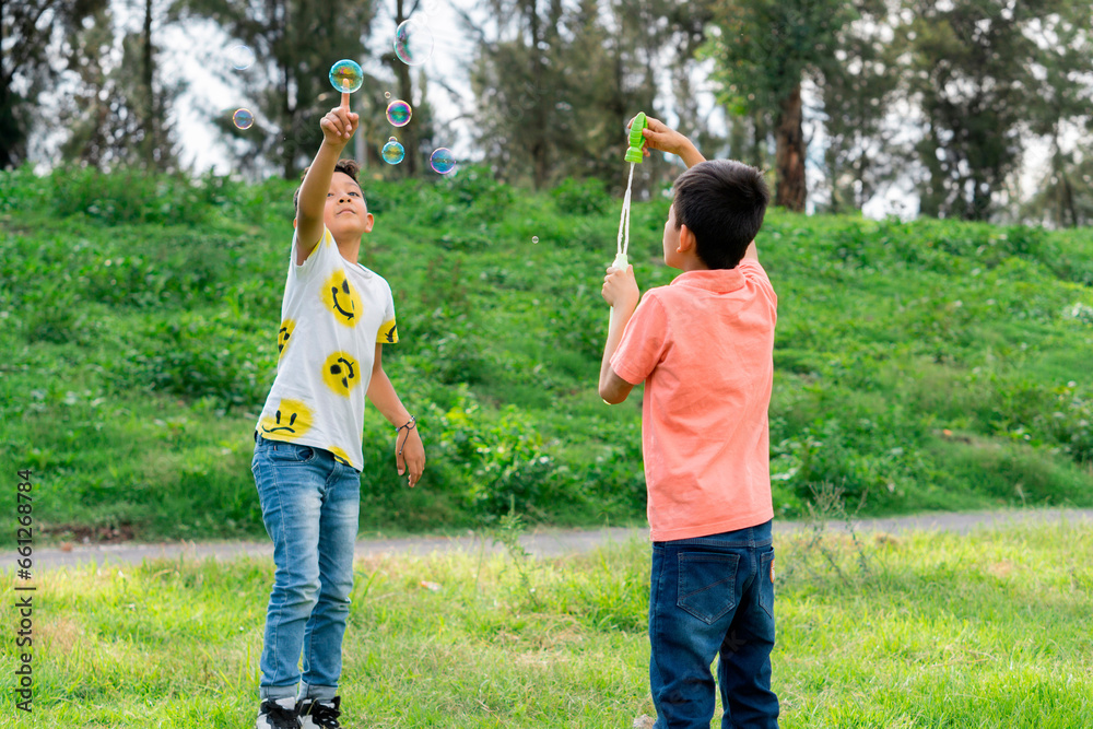 Obraz premium Two children in the park playing with soap bubbles.