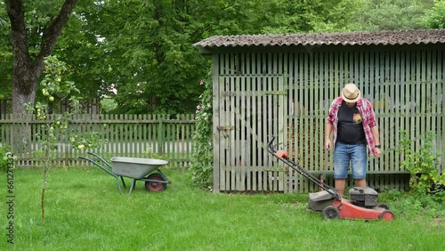 A man in blue jeans starting up lawn mower and cutting grass. The lawn is a lush green color, and it is evenly cut.