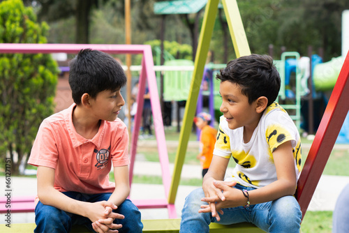Two little Latino friends in the park sitting and talking.