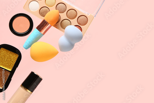 Decorative cosmetics and makeup sponges flying on color background