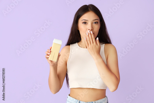 Shocked young Asian woman with liposoluble wax cartridge for epilation on lilac background photo