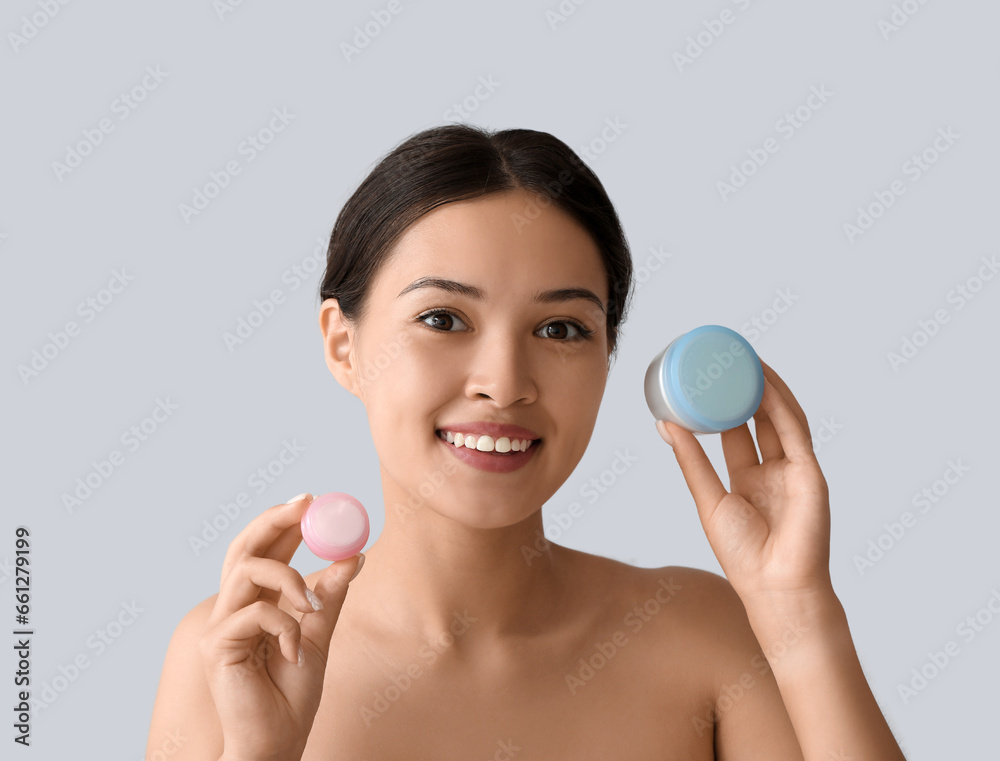 Beautiful Asian woman with jars of cream on light background, closeup Beautiful Asian woman with jars of cream on light background, closeup