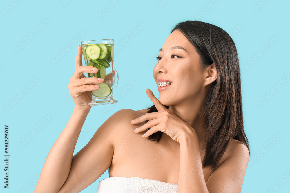 Young Asian woman with glass of cucumber water on blue background Young Asian woman with glass of cucumber water on blue background