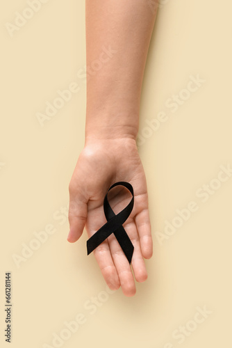 Woman holding black funeral ribbon on beige background