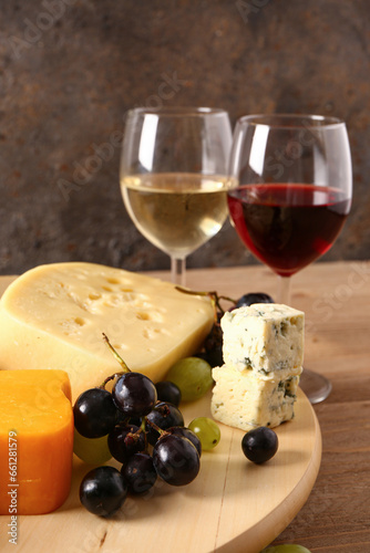 Wooden board with tasty cheese and grapes on table