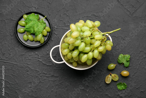 Fresh sweet grapes with leaves in a colander on black background