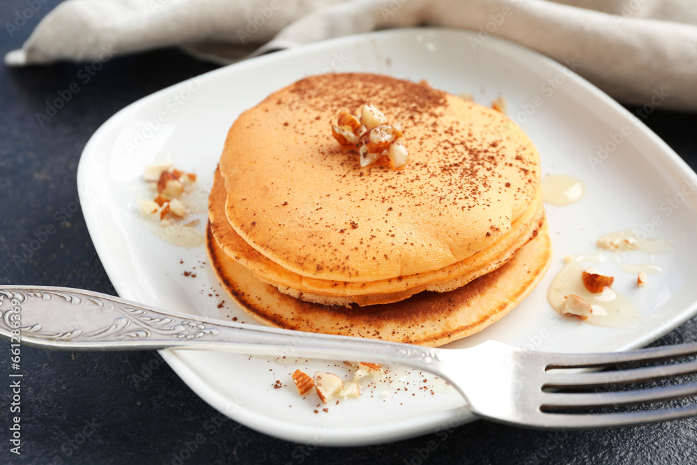 Plate of tasty pumpkin pancakes with cocoa powder and nuts on blue background Plate of tasty pumpkin pancakes with cocoa powder and nuts on blue background