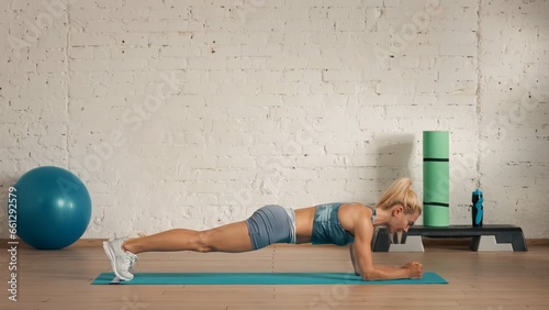 Healthcare creative advertisement concept. Woman fitness coach in the room on the floor standing in elbow plank.