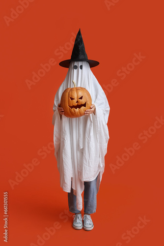 Young woman in Halloween costume of ghost with witch hat and pumpkin on color background