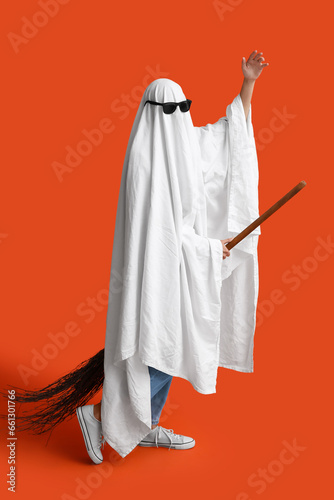 Young woman in Halloween costume of ghost and sunglasses with witch broom on color background