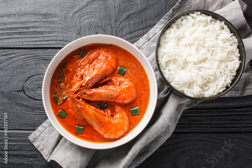 Malai curry dish combines prawns with coconut milk, onion, ginger, garlic paste, tomato, and ground spices and is served with basmati rice closeup on the wooden table. Horizontal top view from above photo