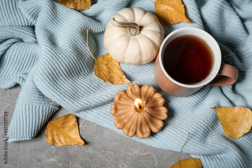 Beautiful composition with burning candle in shape of pumpkin  mug of tea and autumn leaves on grey background