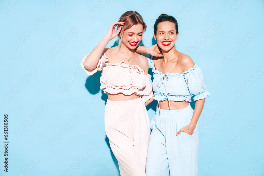 Two young beautiful smiling brunette hipster female in trendy summer clothes. Sexy carefree women isolated near blue wall in studio. Positive models having fun. Cheerful and happy. In sunglasses Two young beautiful smiling brunette hipster female in trendy summer clothes. Sexy carefree women isolated near blue wall in studio. Positive models having fun. Cheerful and happy. In sunglasses