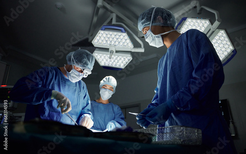 Teamwork, emergency and doctors or people in surgery procedure or healthcare operation in hospital. Night, low angle or surgeon in face mask or gloves help in dark operating room in medical clinic
