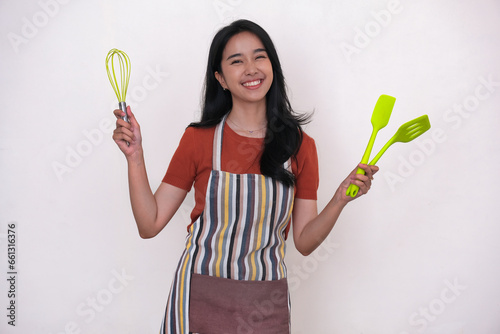 A young Asian woman wearing an apron is holding cooking utensils photo