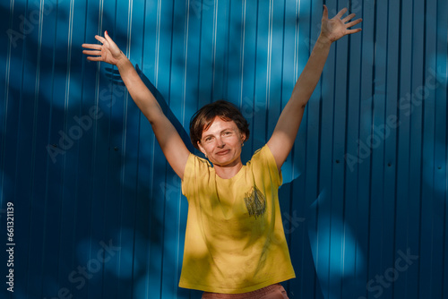 Joyful young brunette woman girl in light casual clothes posing on blue wall background. People emotions lifestyle concept. Mock up copy space. Spreading rising hands