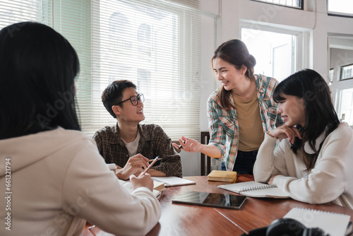 A cheerful and smart young Asian female is standing and sharing her ideas in a meeting with her team. University students, friendship, startups, teamwork