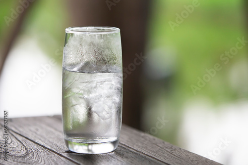 Glass of water with ice on wooden table in the garden, soft focus