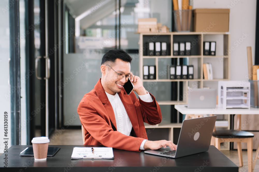 Young handsome man typing on tablet and laptop while sitting at the working wooden table modern office. Young handsome man typing on tablet and laptop while sitting at the working wooden table modern office.