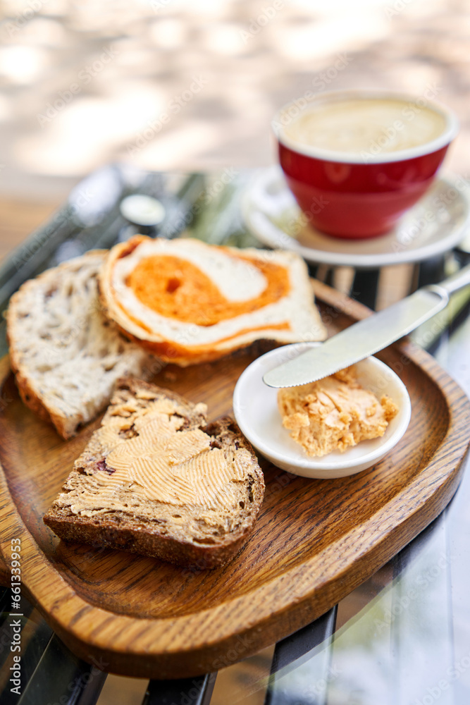 A slice of bread with butter on a chopping board. Assorted sliced bread on a wooden board. Served with smoked butter. Breakfast with cappuccino coffee. 